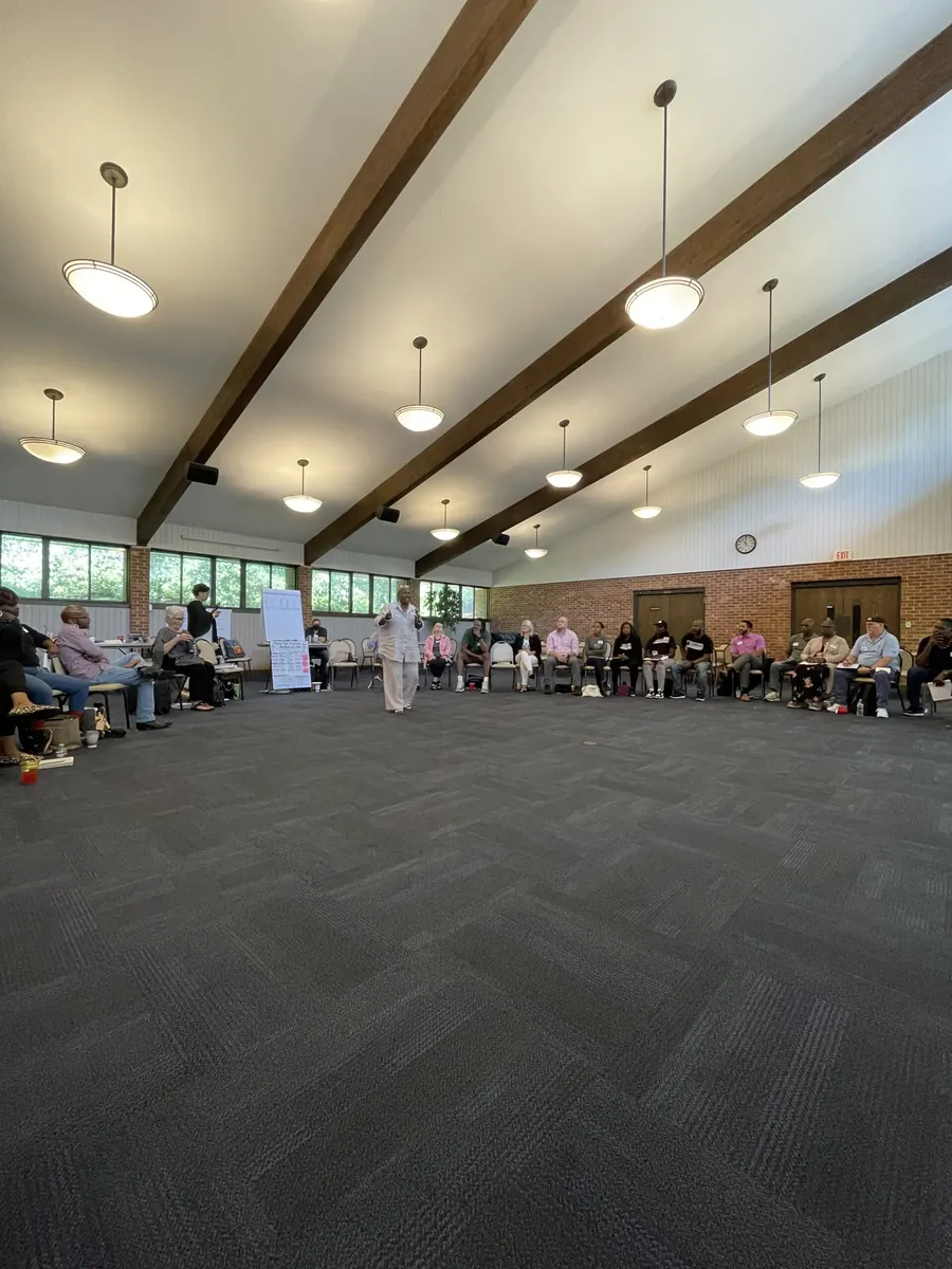 Neighbors seated in a circle in a community meeting hall with exposed wooden beams