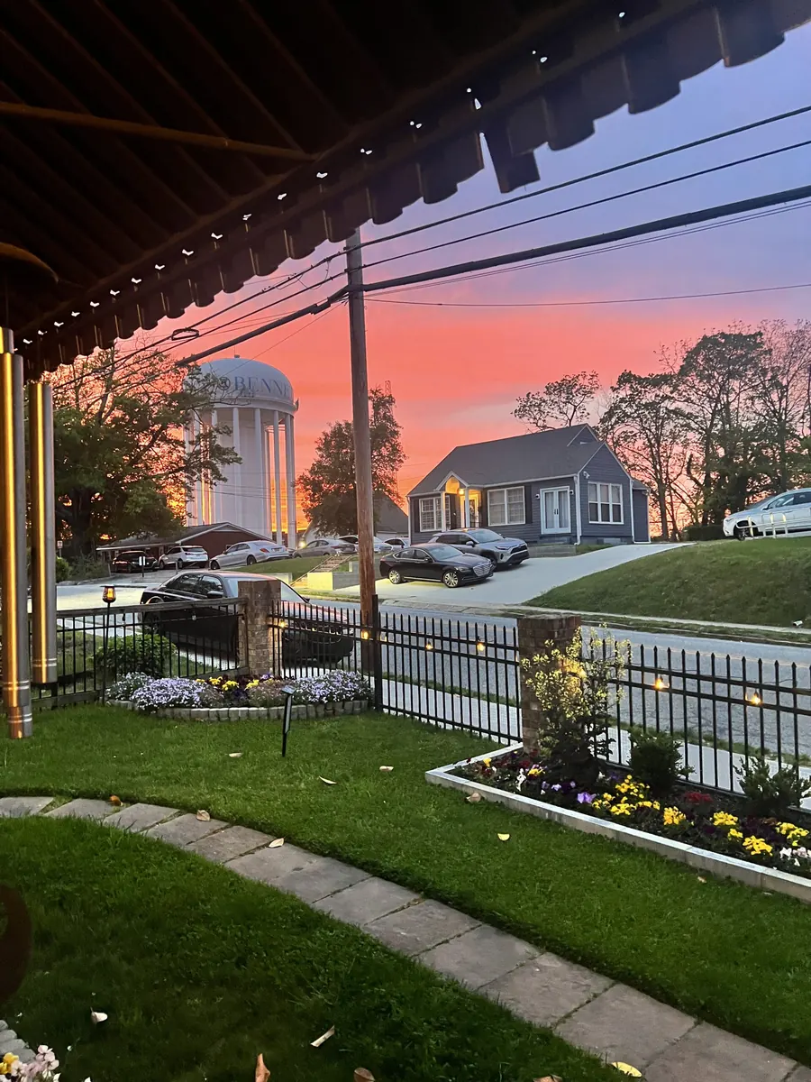 A tended front garden with a white picket fence and a porch at sunset