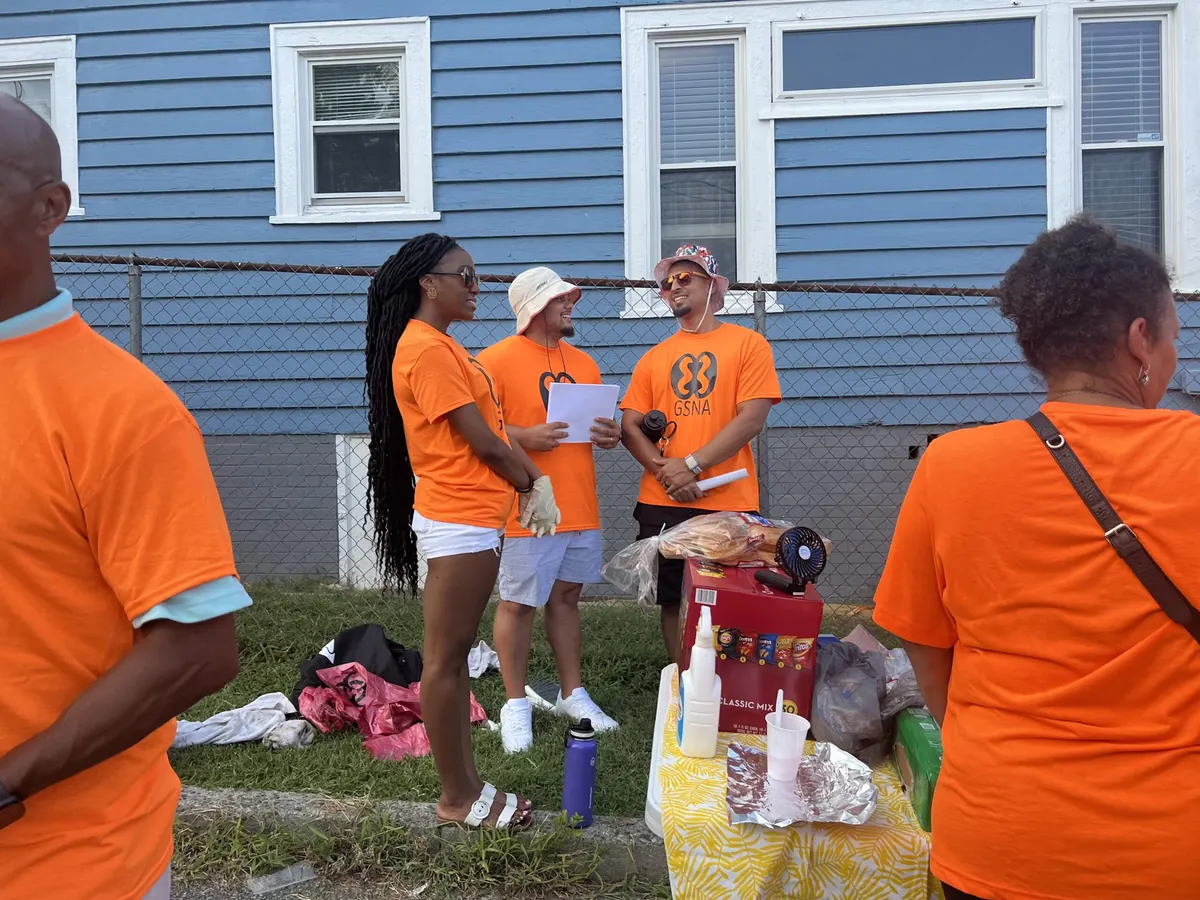 Volunteers in orange neighborhood association shirts gathered outside a blue house